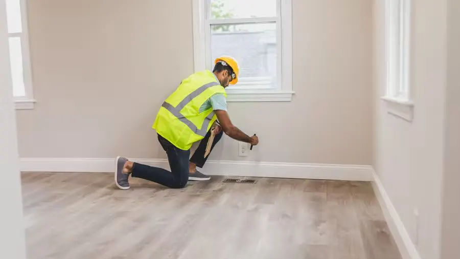A home inspector in high visibility vest examines an electrical outlet in a modern room.